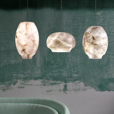 Three alabaster pendant forms glowing against a deep green wall